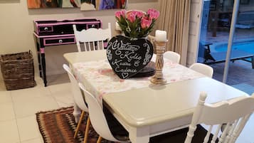 Een eetgedeelte met een tafel gedekt voor vier personen, omringd door witte stoelen met zwarte kussens. Op de tafel staat een zwarte vaas met roze bloemen en een kandelaar.