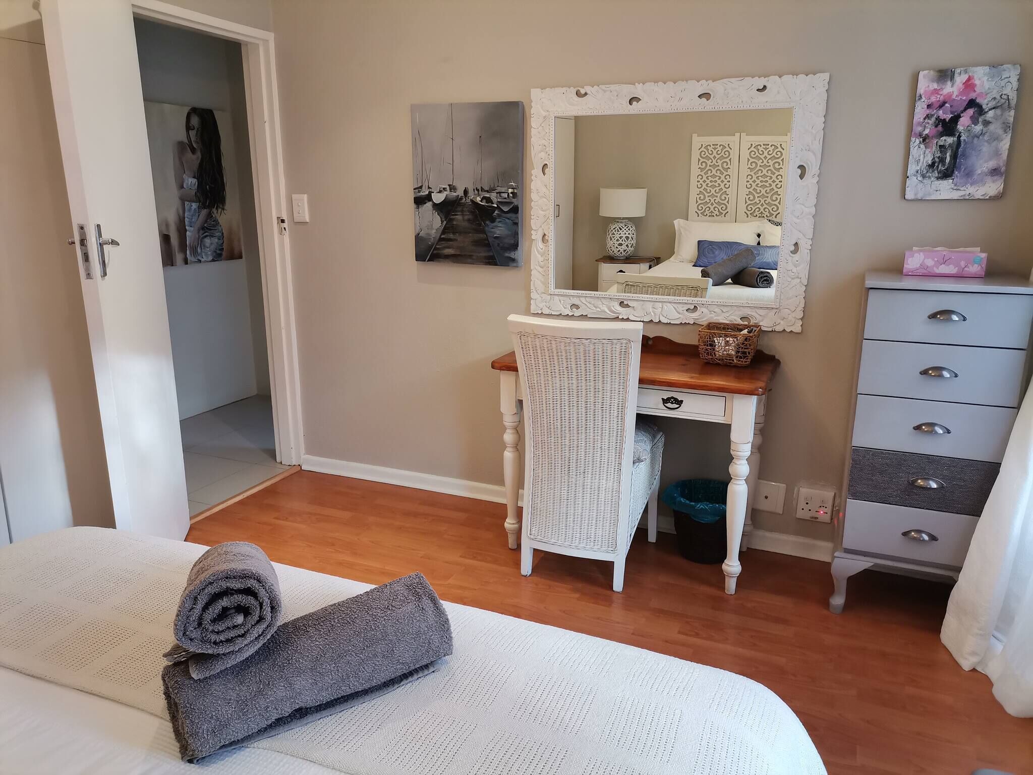 A bedroom with a bed, a dresser, a mirror, and a painting on the wall.