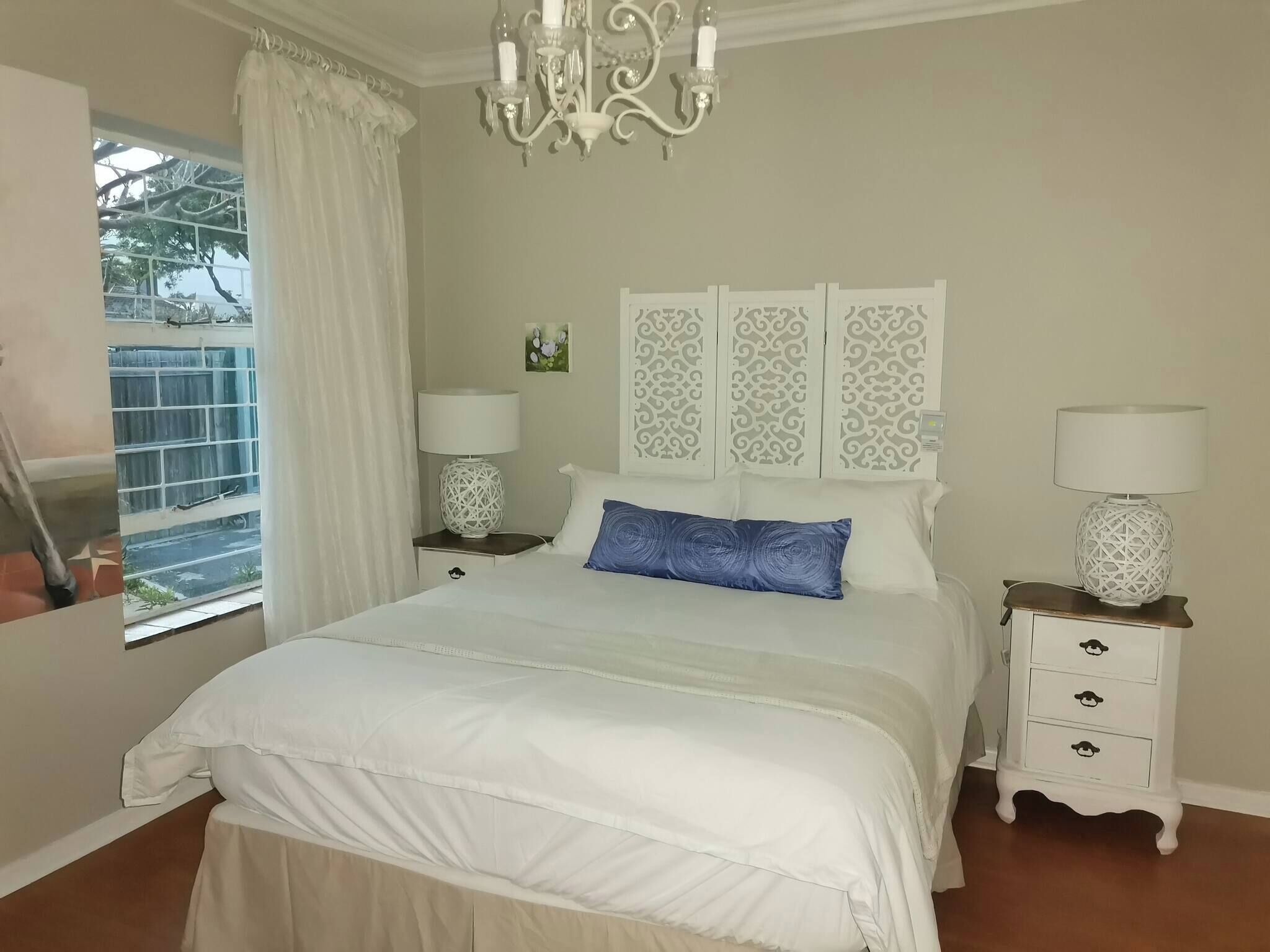 Une chambre à coucher comprenant un lit, des tables de chevet, un lustre et des panneaux décoratifs.