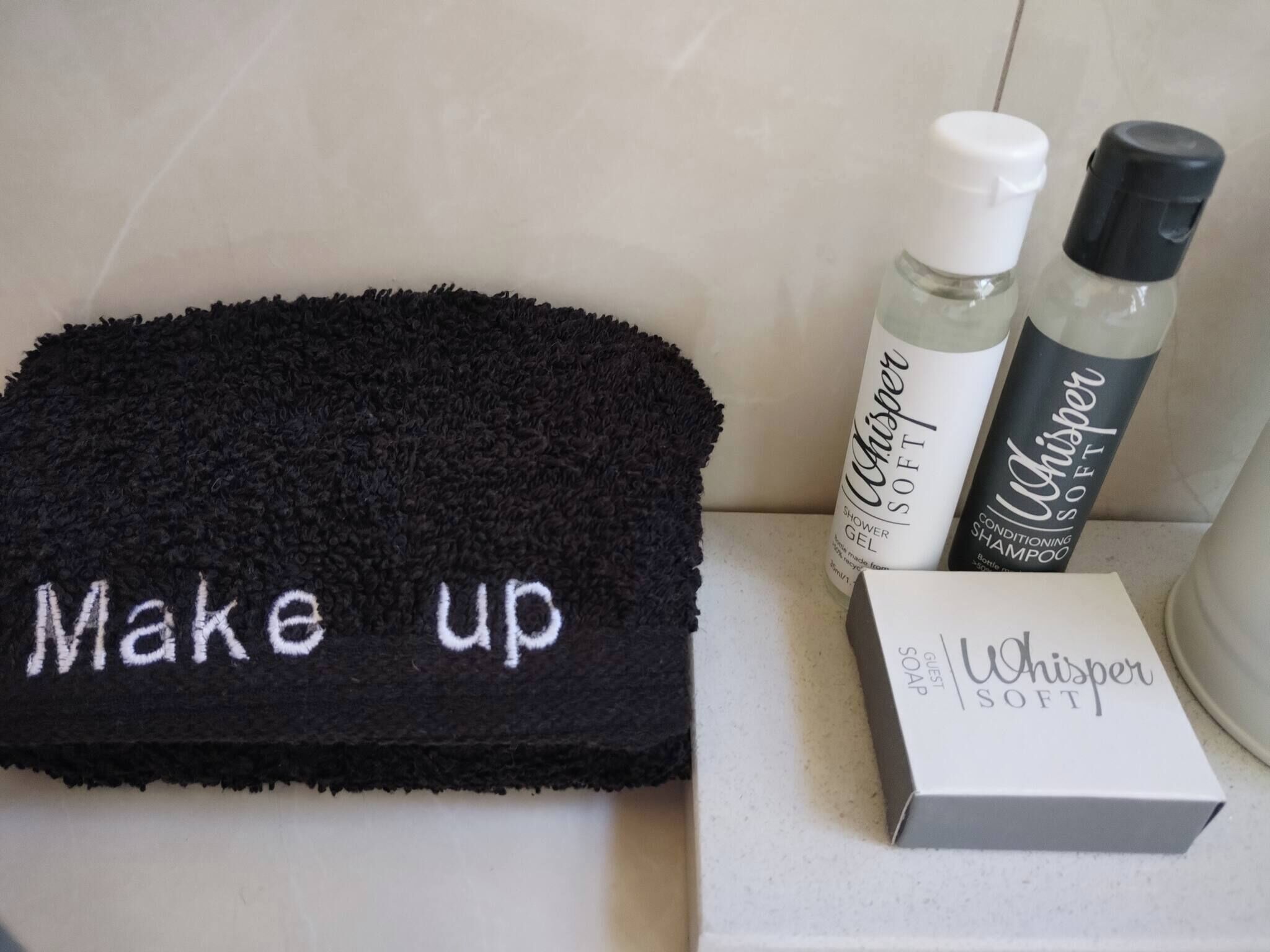 Une serviette noire avec le mot « Maquillage » brodé, un flacon de gel douche, un flacon de shampoing et une boîte de savon.