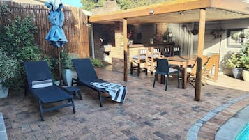 Une terrasse avec une piscine, des chaises longues, une table et une pergola.