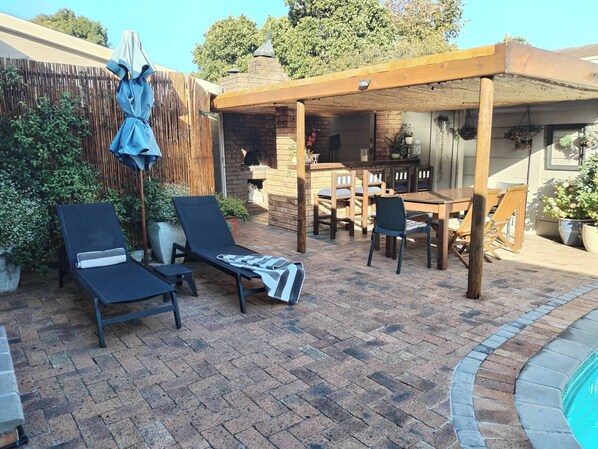 Un patio con piscina, sillas de descanso, una mesa y una pérgola.