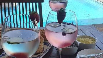 Two cocktails with strawberries on a wooden deck by a pool.