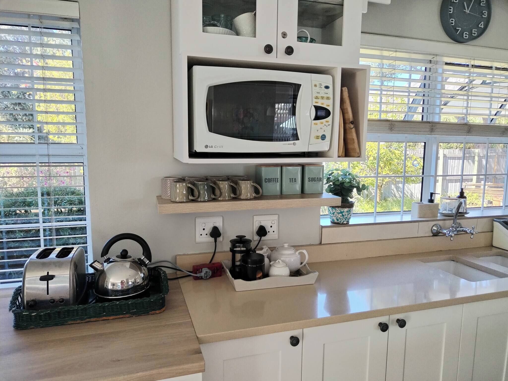 A kitchen with a microwave, toaster, kettle, and coffee maker. There are cabinets above the counter and a window with blinds.
