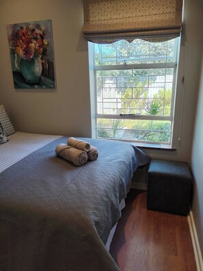 Un dormitorio con cama, ventana con vistas, un cuadro en la pared y una pequeña banca.
