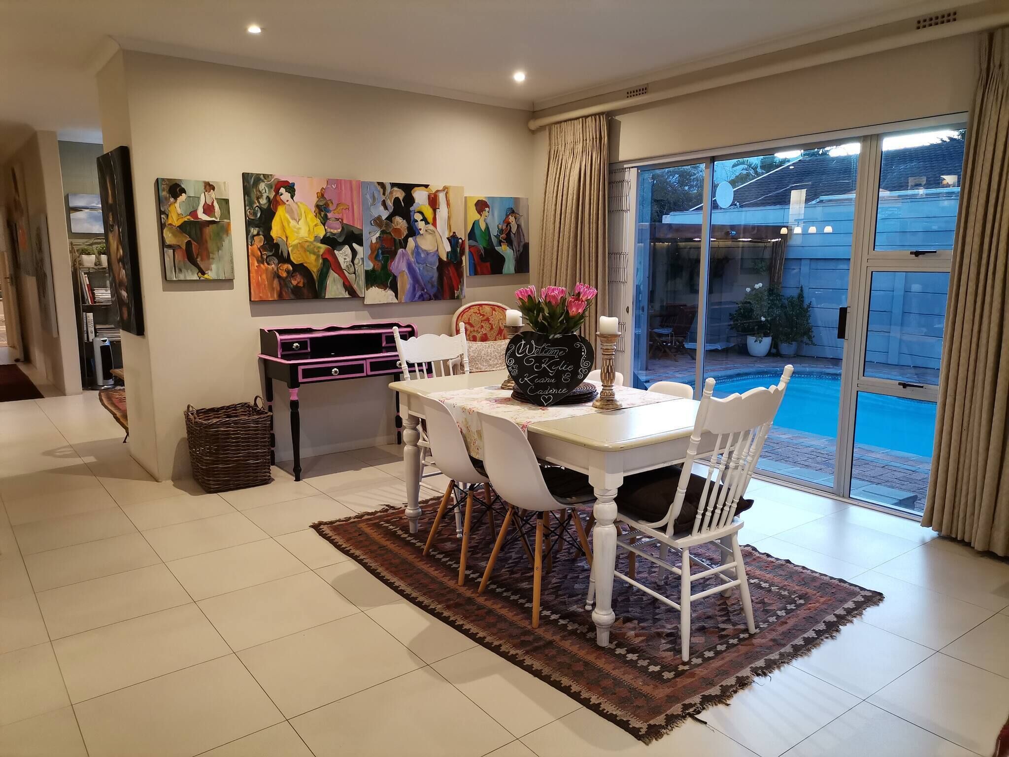 Un coin repas comprenant une table, des chaises, un panneau d’accueil en forme de cœur et une vue sur une piscine, visible à travers de grandes portes vitrées.