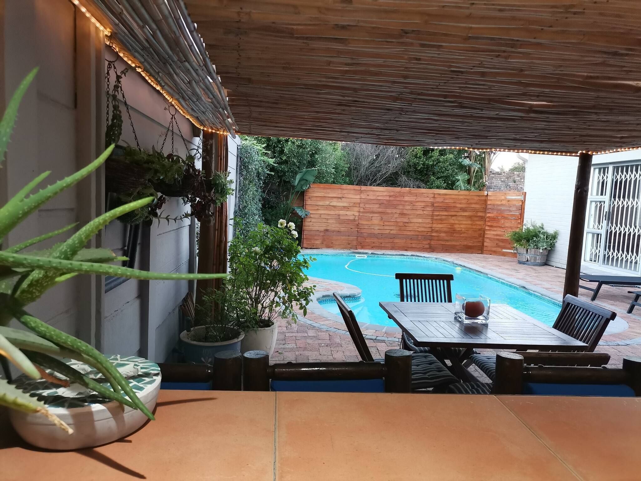 Un patio exterior con piscina, muebles de madera y plantas en macetas.
