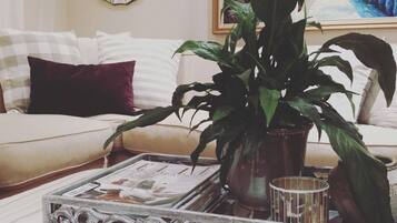 A living room with a sofa, a potted plant, a tray with magazines, and a decorative mirror.