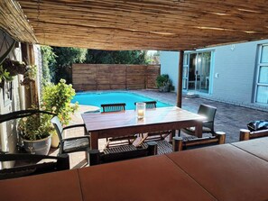 Une terrasse extérieure avec une piscine, une table en bois, des chaises et des plantes en pot.