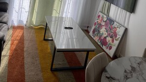 Ein Zimmer mit einem Bett, einem Tisch, einem Sessel, einem an der Wand befestigten Fernseher und einem Fenster mit Vorhängen.