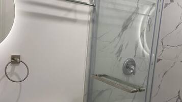 A modern bathroom with a glass-enclosed shower, a toilet, and a towel rack.