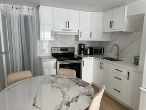 A compact kitchen with white cabinets, a stove, a microwave, and a sink. - Oshawa Suite Open Kitchen Living Space (Oshawa)