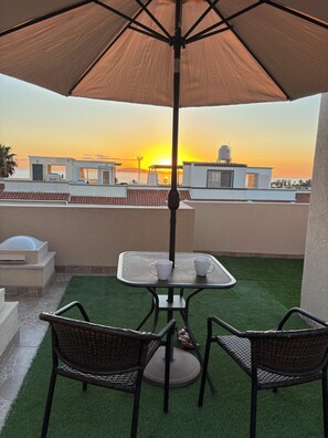 A rooftop terrace with a table and chairs, an umbrella, and a view of the sunset over the sea. - Ocean Sunset Views • Rooftop Patio • Entire Home Near Rosarito Beach (Brisas del Mar)