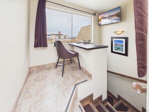 A small room with a window, a chair, a flat-screen TV mounted on the wall, and a framed picture.