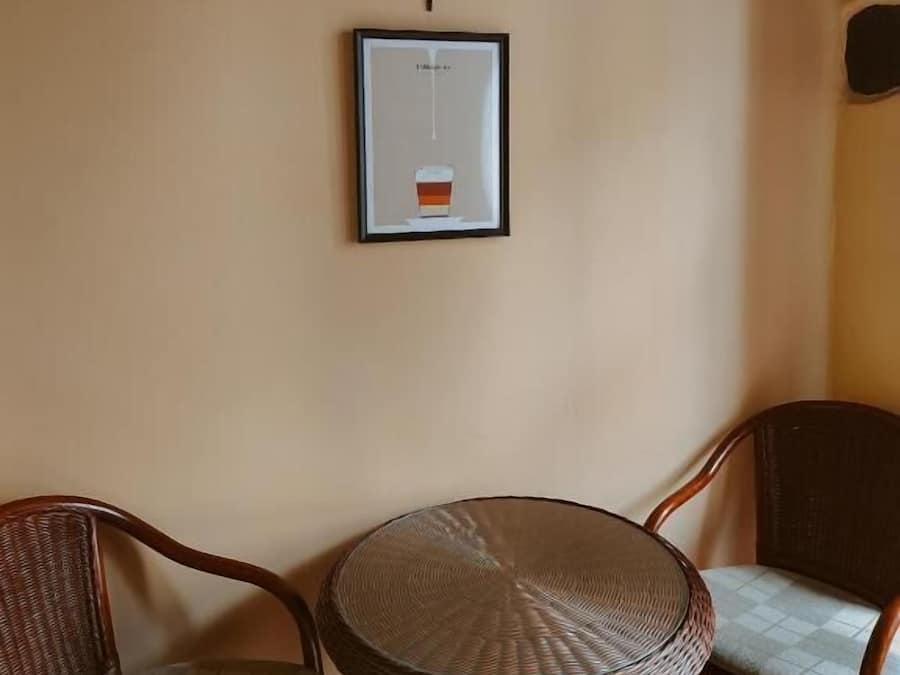 A room with a round wicker table, two wicker chairs, a framed picture, and a wall-mounted candle holder.