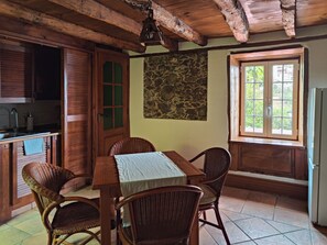 Un comedor rústico con una mesa de madera, sillas de mimbre, una pared de piedra y una ventana con vistas.