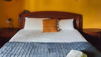 Un letto con una coperta blu, una testiera in legno e un muro giallo con un applique.