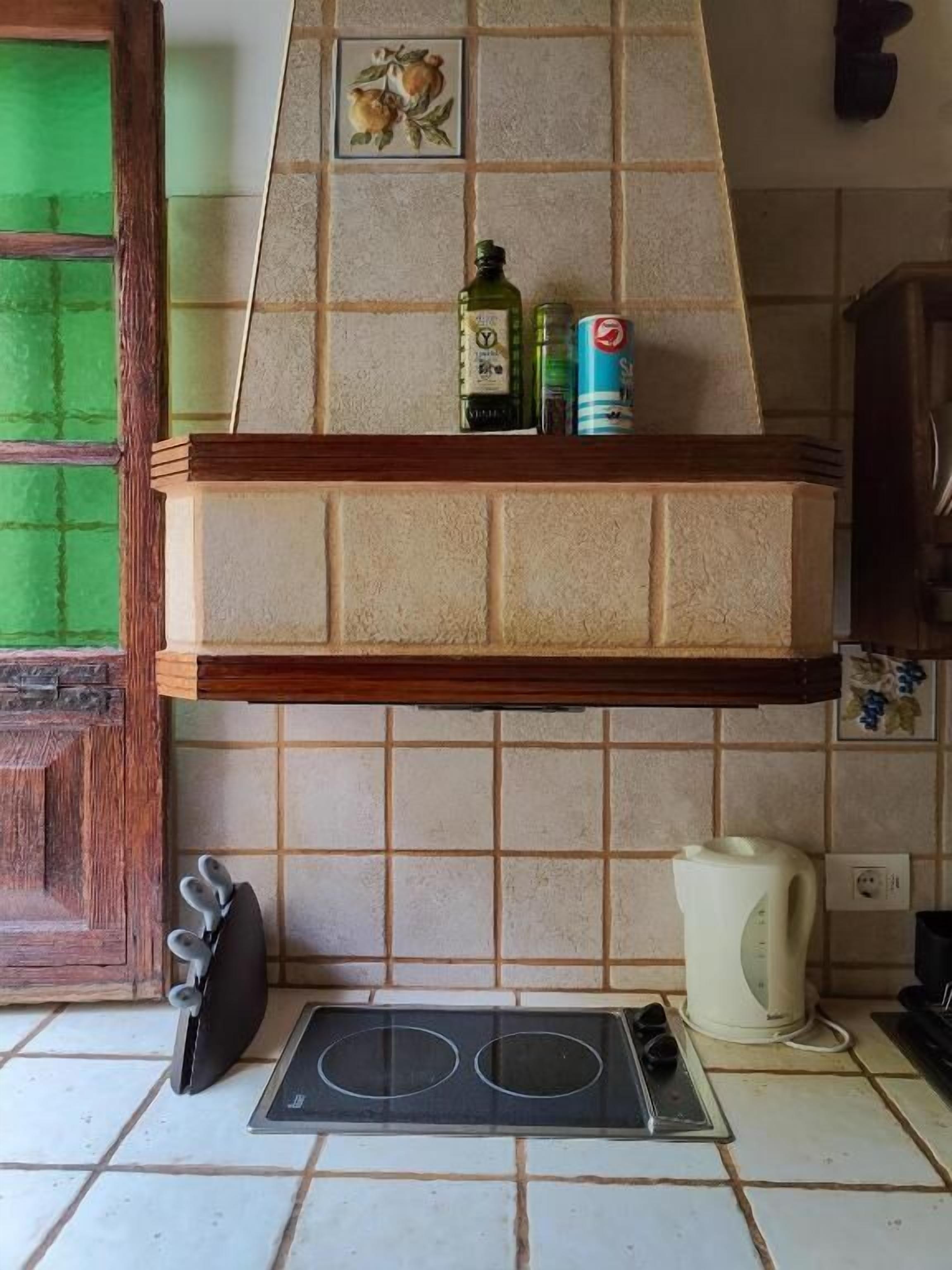 Une cuisine équipée d’une cuisinière intégrée, d’une machine à café et d’une étagère où sont rangées des bouteilles et des conserves.