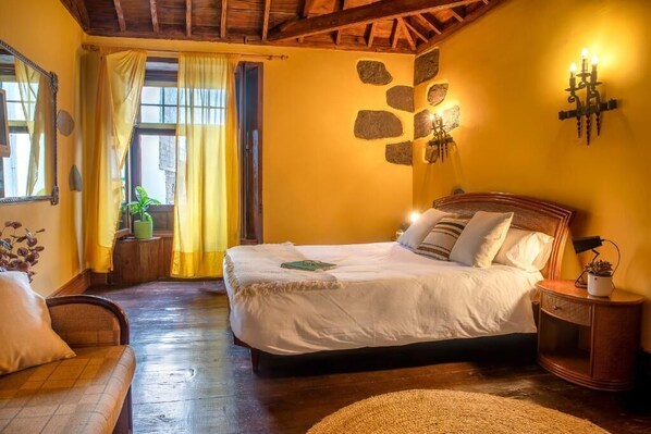 Un dormitorio con cama, cabecera de madera, mesita de noche, ventana con cortinas y decoración de pared de piedra.
