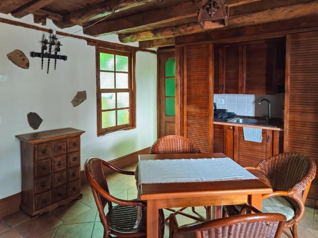 A rustic kitchen with wooden cabinets, a dining table with chairs, and a window with green-tinted glass.