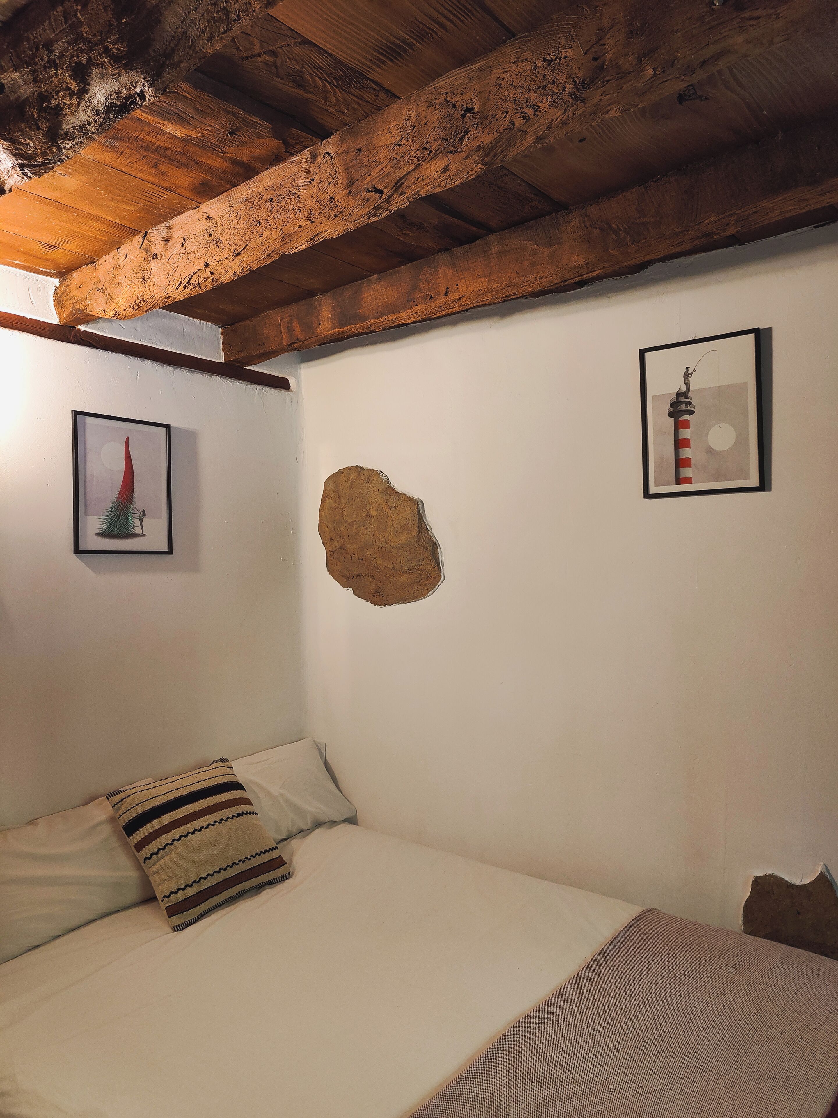 Una camera da letto con un letto, un cuscino, un quadro incorniciato e una parete con un buco.