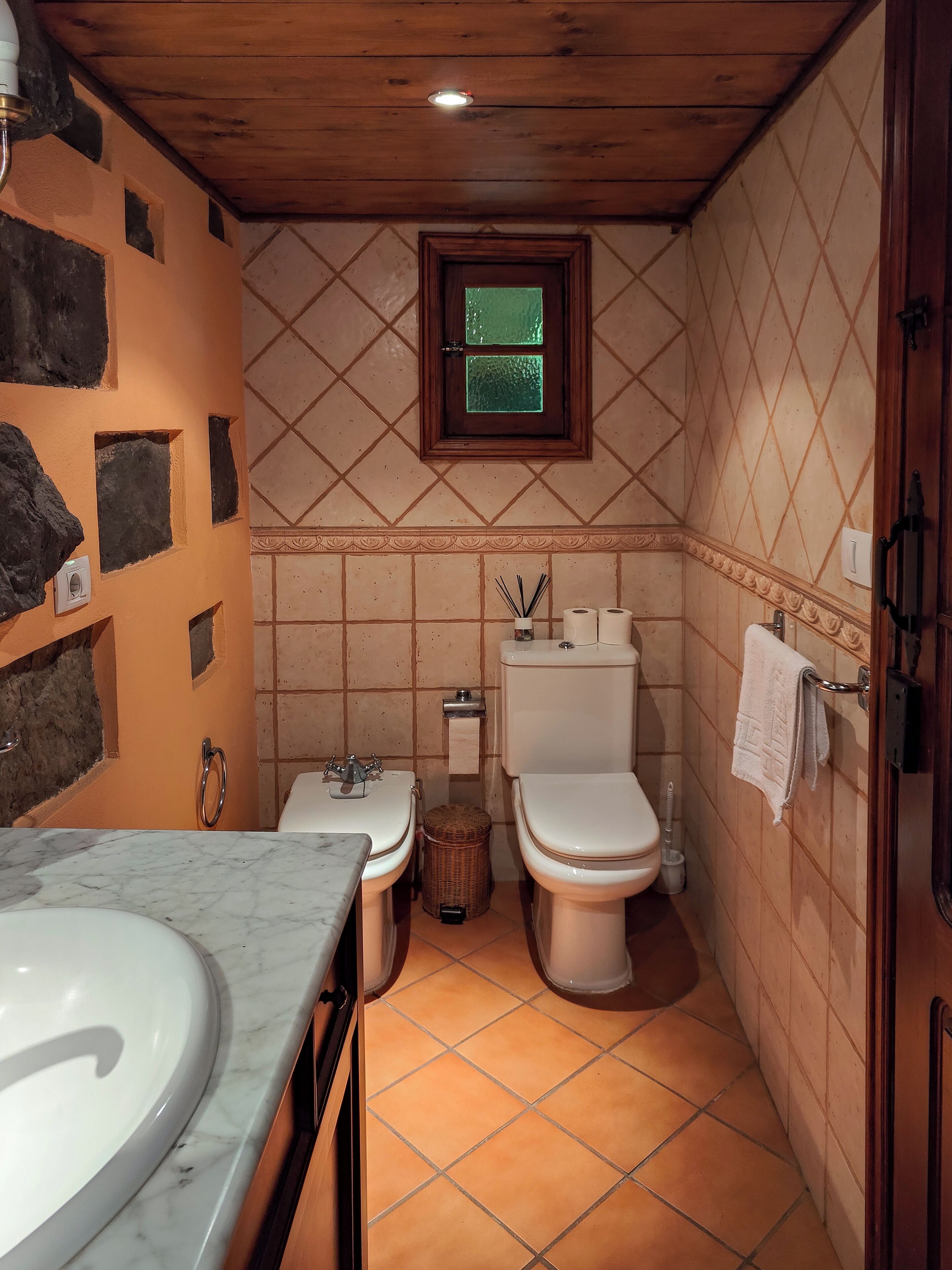Een badkamer met een marmeren wastafel, twee toiletten, een raam en een houten plafond.
