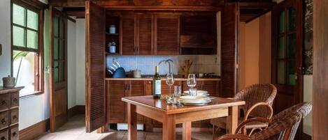 Une cuisine rustique avec des meubles en bois, une table à manger dressée pour deux personnes et des chaises en osier.
