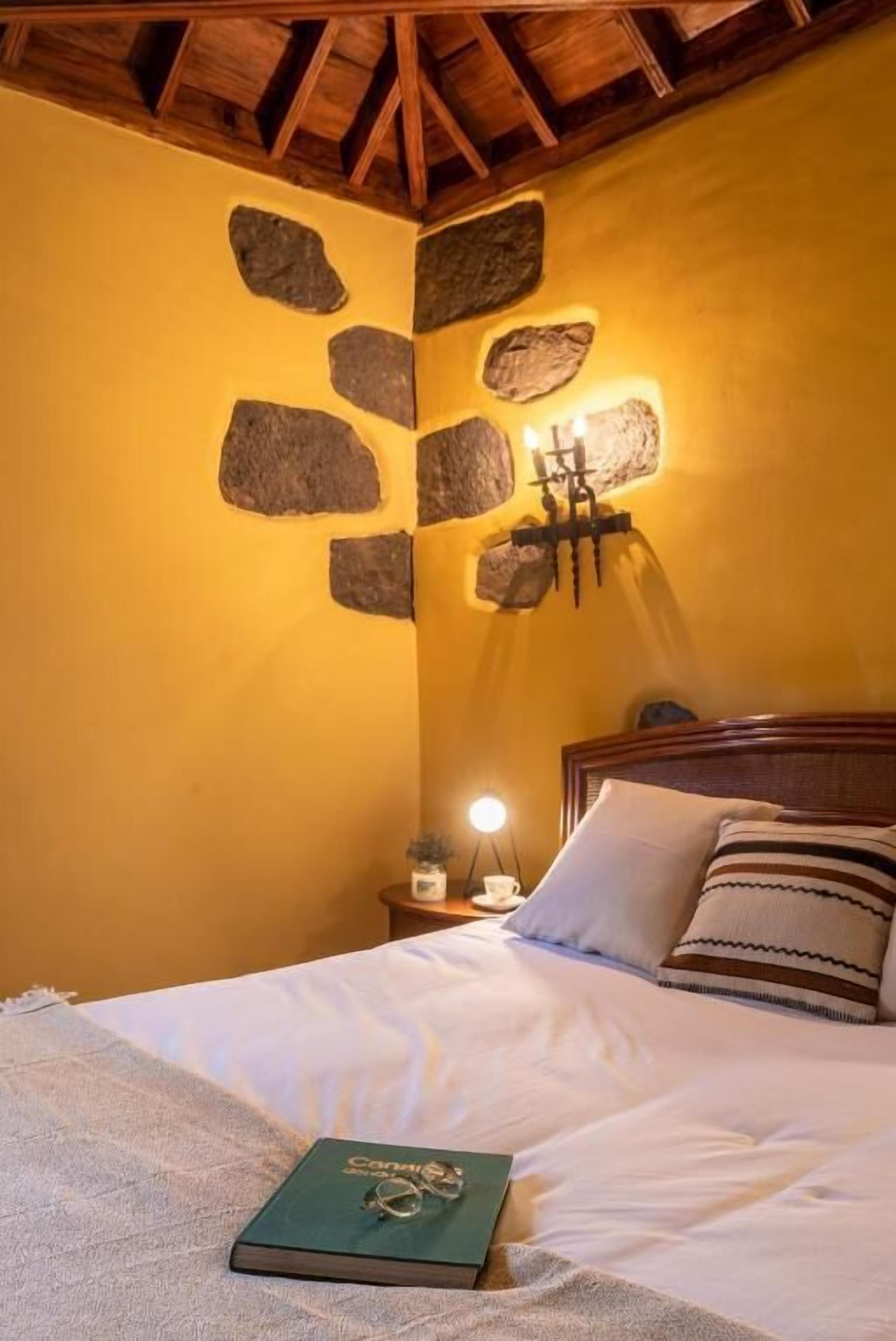 A bed with a book, a pillow, and a wall-mounted light fixture.