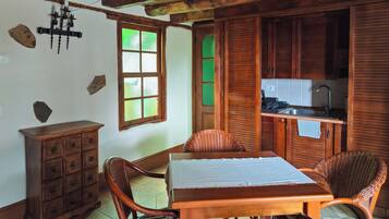 Una mesa de comedor de madera con sillas, un armario de madera, un ventanal con vidrio esmerilado y una zona de cocina con armarios de madera y un lavamanos.