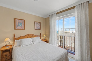 A hotel room with a bed, two bedside tables, a nightstand, a window with a view, and two framed pictures on the wall. - 'Duplex by the Sea' Apartment with WiFi and Air Conditioning (Torremolinos)