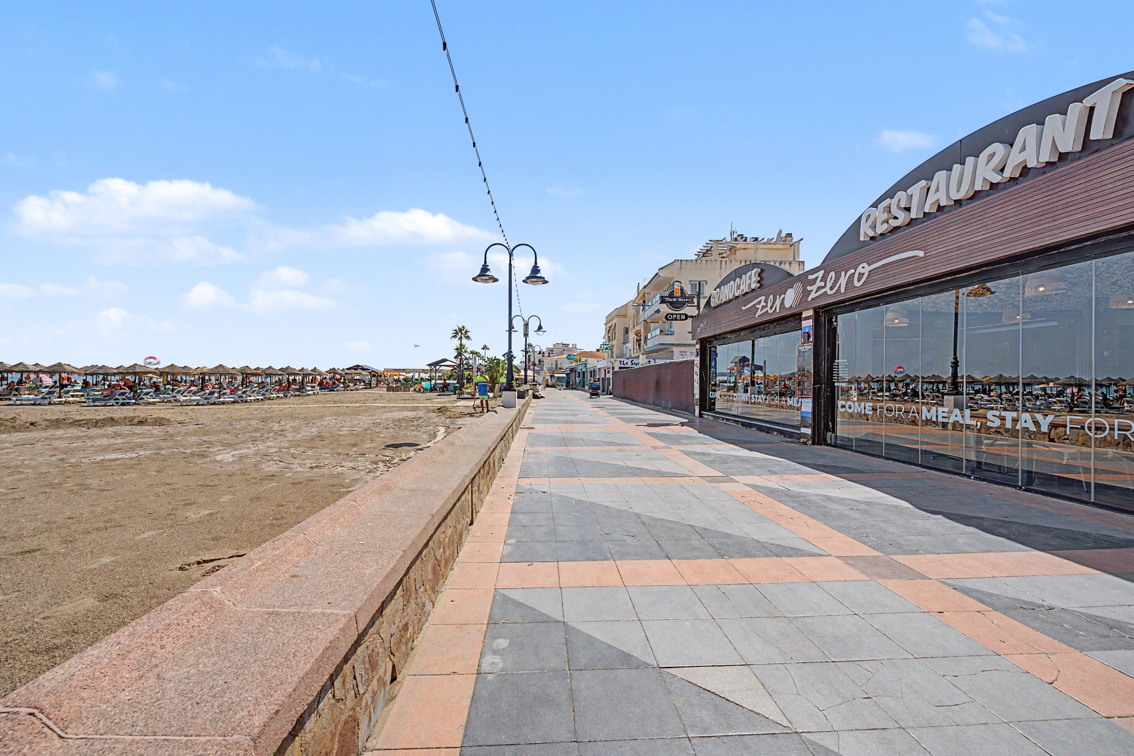 Una passeggiata lungomare con un ristorante chiamato 'GRANOCAFE Zero' e un cartello per il caffè 'The Sun'.