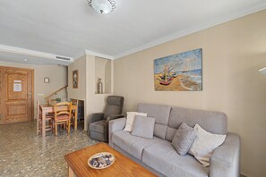 A living room with a grey sofa, a wooden coffee table, and a painting of boats on the wall. - 'Duplex by the Sea' Apartment with WiFi and Air Conditioning (Torremolinos)