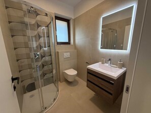 Ein modernes Badezimmer mit Duschkabine aus Glas, Toilette, Waschbecken mit Spiegel und Fenster.