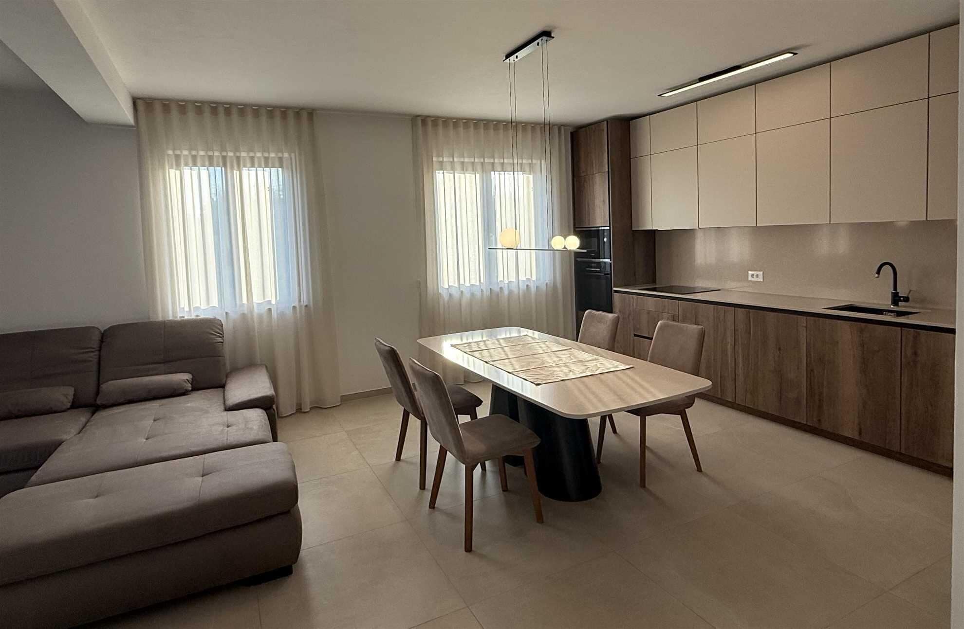 Een moderne woonkamer met een bank, een eettafel met stoelen en een keuken met kasten en een spoelbak.