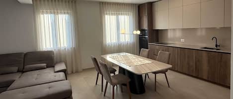 Een moderne woonkamer met een bank, een eettafel met stoelen en een keuken met kasten en een spoelbak.