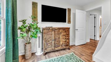 Un couloir avec une armoire en bois, une plante en pot, un téléviseur à écran plat et un tapis à motifs.