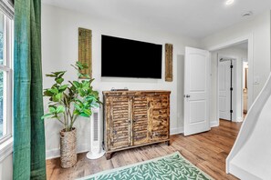 A hallway with a wooden cabinet, a potted plant, a flat-screen TV, and a patterned rug.