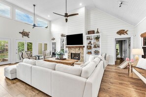 A spacious living room with a large white sofa, a fireplace, and a television mounted on the wall.
