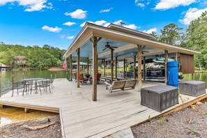 A covered outdoor deck with tables and chairs, a swing, and a view of a lake.