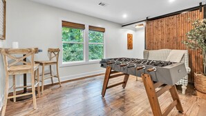 A room with a foosball table, wooden chairs, a window with a view of greenery, and a wooden wall. - Premier Lake Martin Lakefront Home with Private Boat Ramp, 38 Minutes to Auburn! (Dadeville)