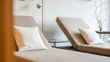 Two lounge chairs with white cushions, a glass table, and a wall-mounted light fixture.