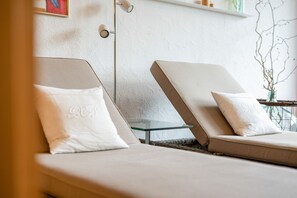 Zwei Liegestühle mit weißen Kissen, ein Glastisch und eine wandmontierte Leuchte.