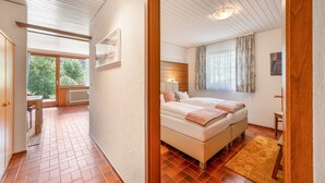 Ein Schlafzimmer mit einem großen Bett, einem Fenster mit Vorhängen und Blick ins Freie.