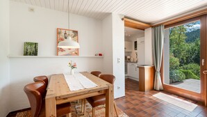 Ein Essbereich mit einem Holztisch, Stühlen, einer Hängelampe sowie Blick auf eine Küche und einen Garten durch eine Glastür.