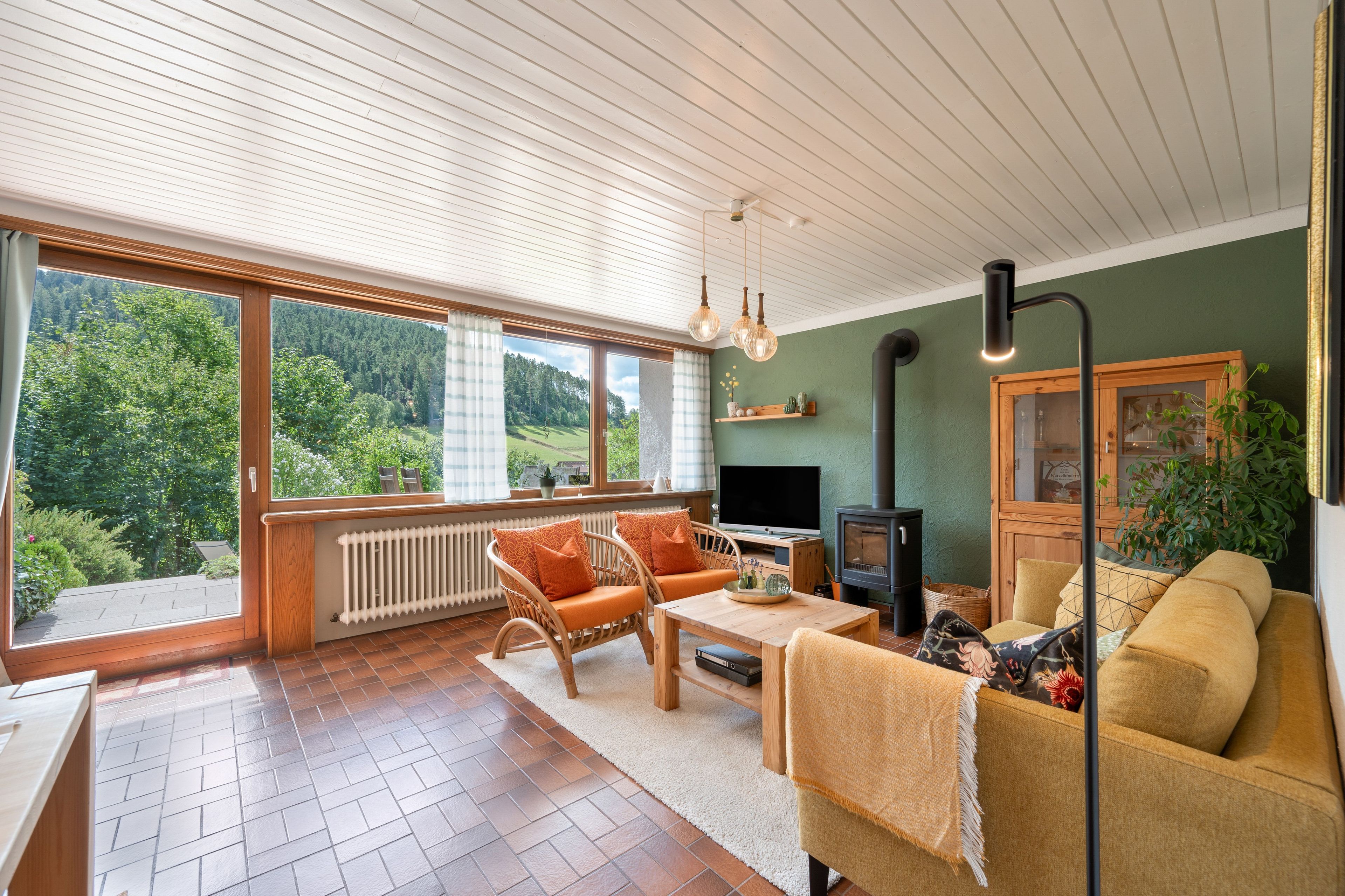 Ein gemütliches Wohnzimmer mit Kamin, großen Fenstern und Blick ins Freie.