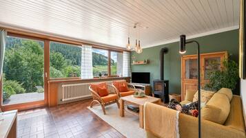 Ein gemütliches Wohnzimmer mit Kamin, großen Fenstern und Blick ins Freie.