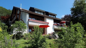 Ein modernes, zweistöckiges Haus mit Balkon, umgeben von üppigem Grün und einem Garten.