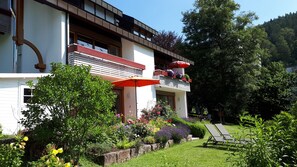 Ein zweigeschossiges Gebäude mit Balkon, Außenbestuhlung und einem Garten.