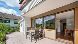 Ein modernes Haus mit Terrasse, einem Essbereich inklusive Tisch und Stühlen und Blick auf die umliegende Landschaft.