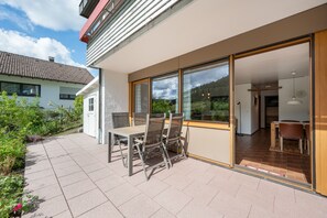 Ein modernes Haus mit Terrasse, einem Essbereich inklusive Tisch und Stühlen und Blick auf die umliegende Landschaft.
